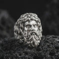 Load image into Gallery viewer, Polished 925 sterling silver Poseidon ring resting on black volcanic stone, highlighting the detailed Greek god portrait, expressive facial features, curled mustache, flowing sculptural hair, and bright polished silver finish.