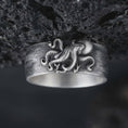 Load image into Gallery viewer, Oxidized 925 sterling silver octopus tentacle ring displayed against textured black volcanic rock, featuring a sculpted octopus with curling arms, raised suction cups, flowing tentacles, wide band design, and dark oxidized silver finish.