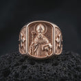 Load image into Gallery viewer, Rose gold plated 925 sterling silver Saint Nicholas of Myra ring resting on black volcanic stone, highlighting the raised bishop portrait, ornate mitre, halo, pastoral staff, symbolic three-ball book, geometric background, and warm rose gold plated finish.