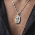 Load image into Gallery viewer, Polished Silver St Paul necklace hanging on a man's chest, highlighting the sculptural saint portrait and oval medallion design.
