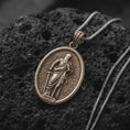 Load image into Gallery viewer, Bronze Saint Paul Apostle pendant on black volcanic rock, featuring the haloed saint holding a sword and book in detailed relief.