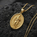 Load image into Gallery viewer, Gold Plated Saint Paul Apostle pendant displayed on black volcanic rock, showing the sculpted robes, sword, and cross-decorated bail.