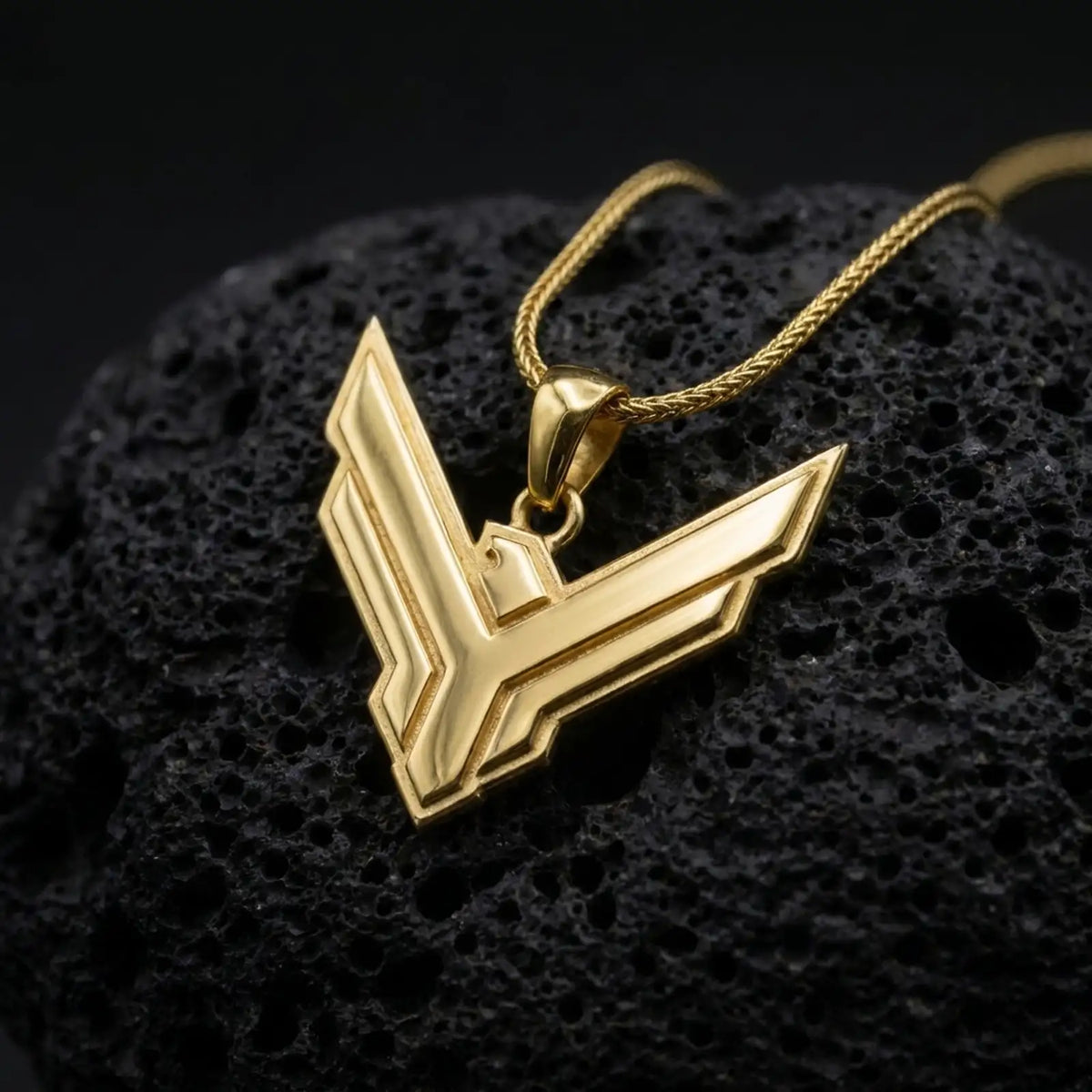Gold plated House Atreides pendant resting on black volcanic rock, featuring the iconic hawk emblem, angular geometric lines, and bold Dune inspired necklace design.