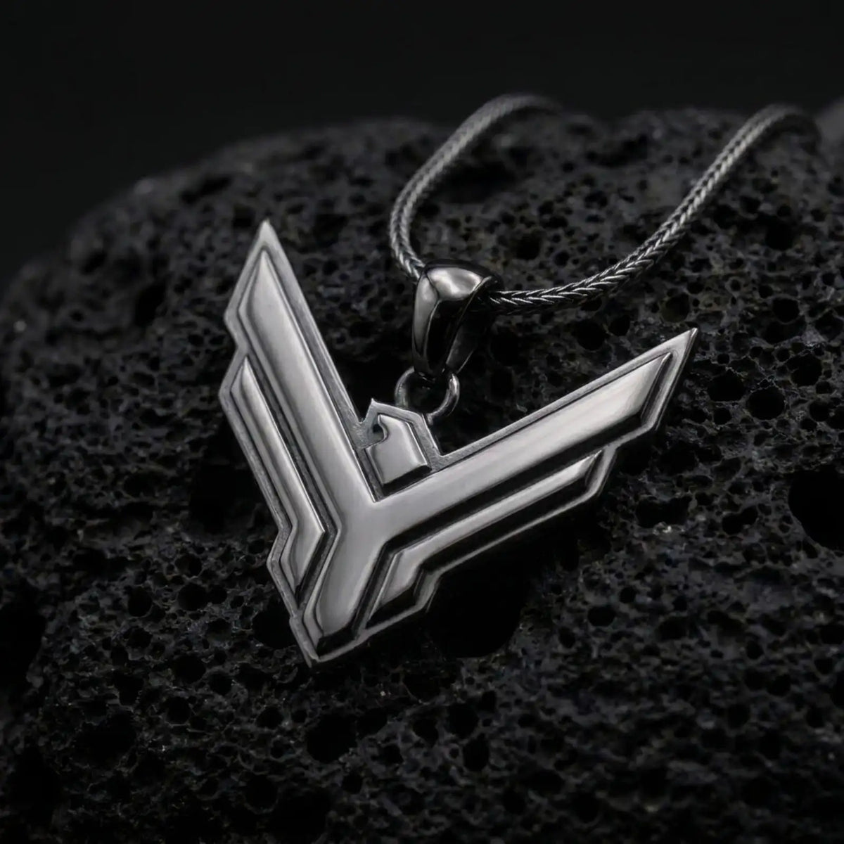 Black rhodium plated House Atreides necklace displayed on textured volcanic stone, showcasing the stylized hawk symbol, layered edges, and distinctive science fiction aesthetic.