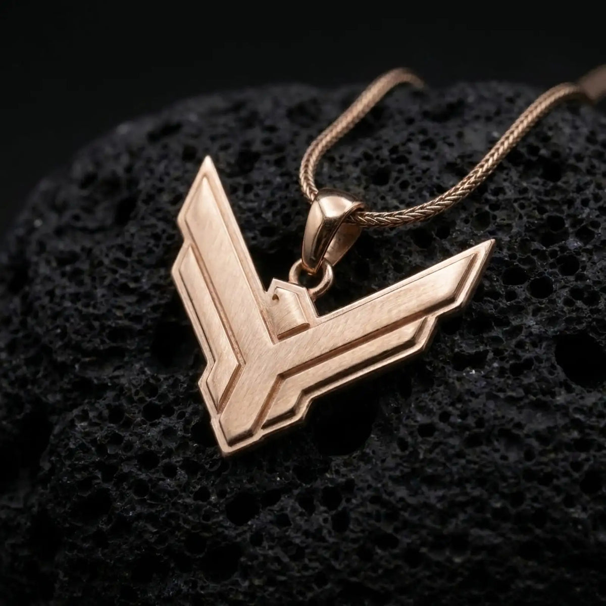 Rose gold plated House Atreides necklace displayed on textured volcanic stone, showcasing the stylized hawk symbol, layered edges, and distinctive science fiction aesthetic.