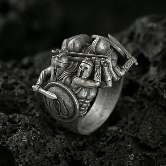 Sterling silver Spartan warrior ring with an oxidized finish, sculptural battle scene featuring armored Greek soldiers, shield and sword detail, macro on black volcanic rock