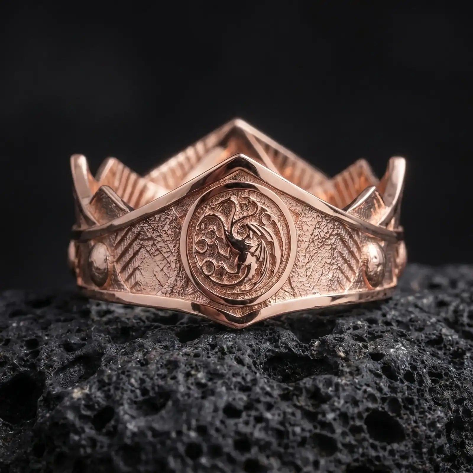Rose gold plated Targaryen dragon ring on textured volcanic rock, detailed macro product shot with soft warm reflections and bold fantasy house symbolism.