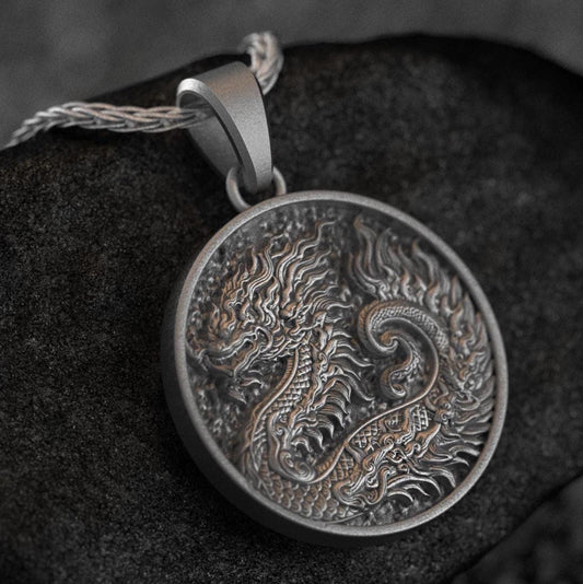 Antique silver Azure Dragon medallion pendant resting on dark stone background,