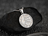 Silver Chinese dragon medallion pendant with baroque oriental details on dark stone background,