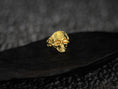 Load image into Gallery viewer, Front view of gold-plated skull ring with fleur-de-lis detail.
