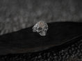 Load image into Gallery viewer, Angled view of ornate silver skull ring on textured pedestal.
