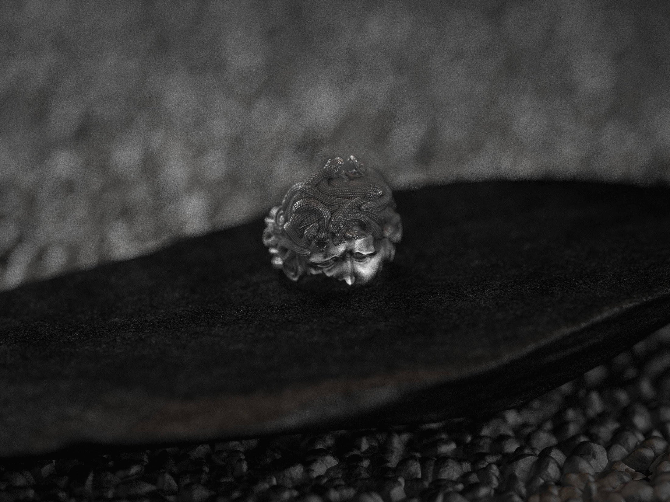 Angled view of silver Medusa ring on dark stone.