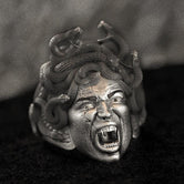 Close-up of sterling silver Medusa signet ring on black stone.