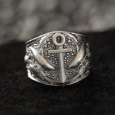 Close-up of sterling silver anchor and sharks signet ring on black stone.