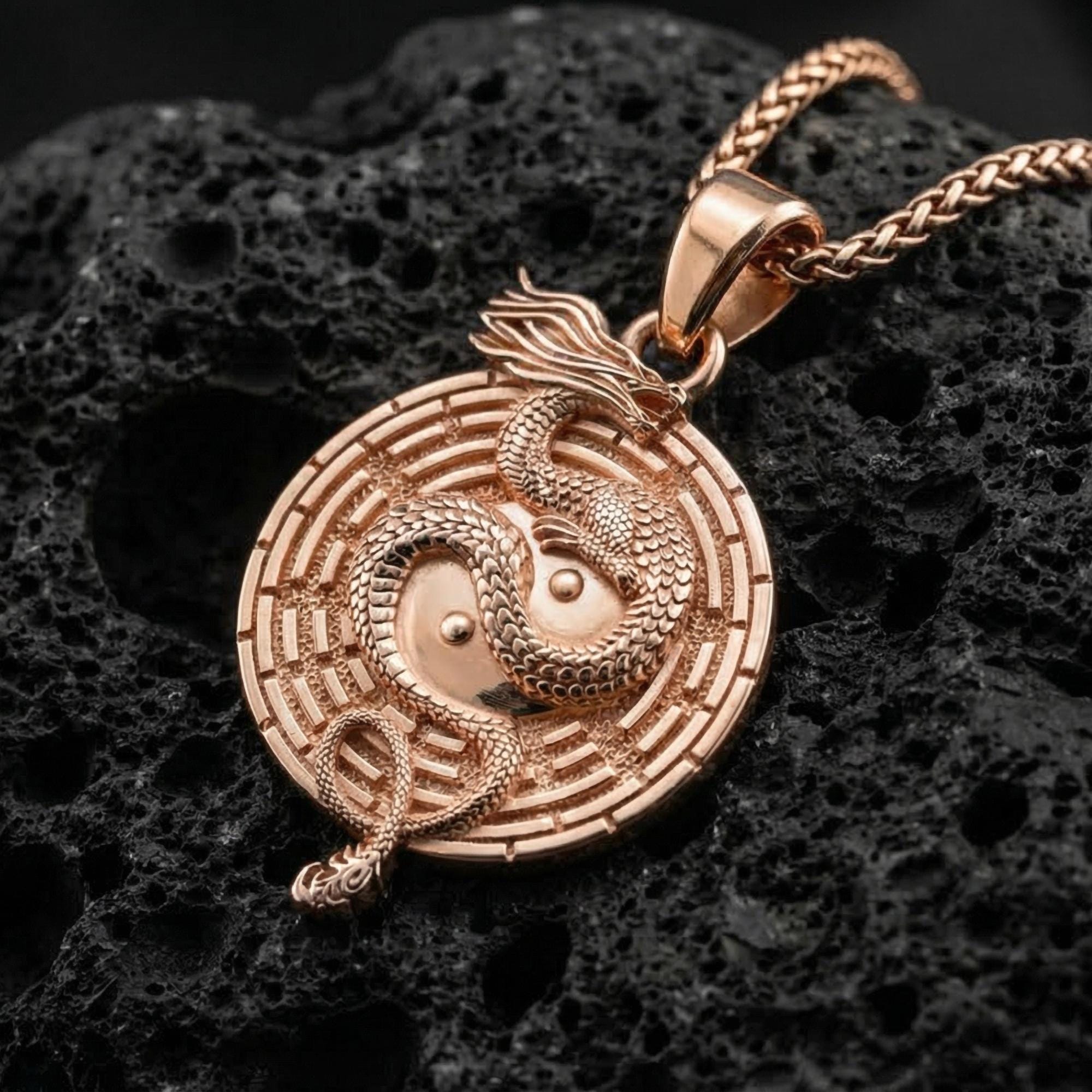 Rose gold plated yin yang dragon medallion necklace with symbolic maze border on volcanic rock surface