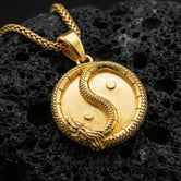 Gold plated yin yang dragon pendant necklace symbolizing balance on volcanic stone surface