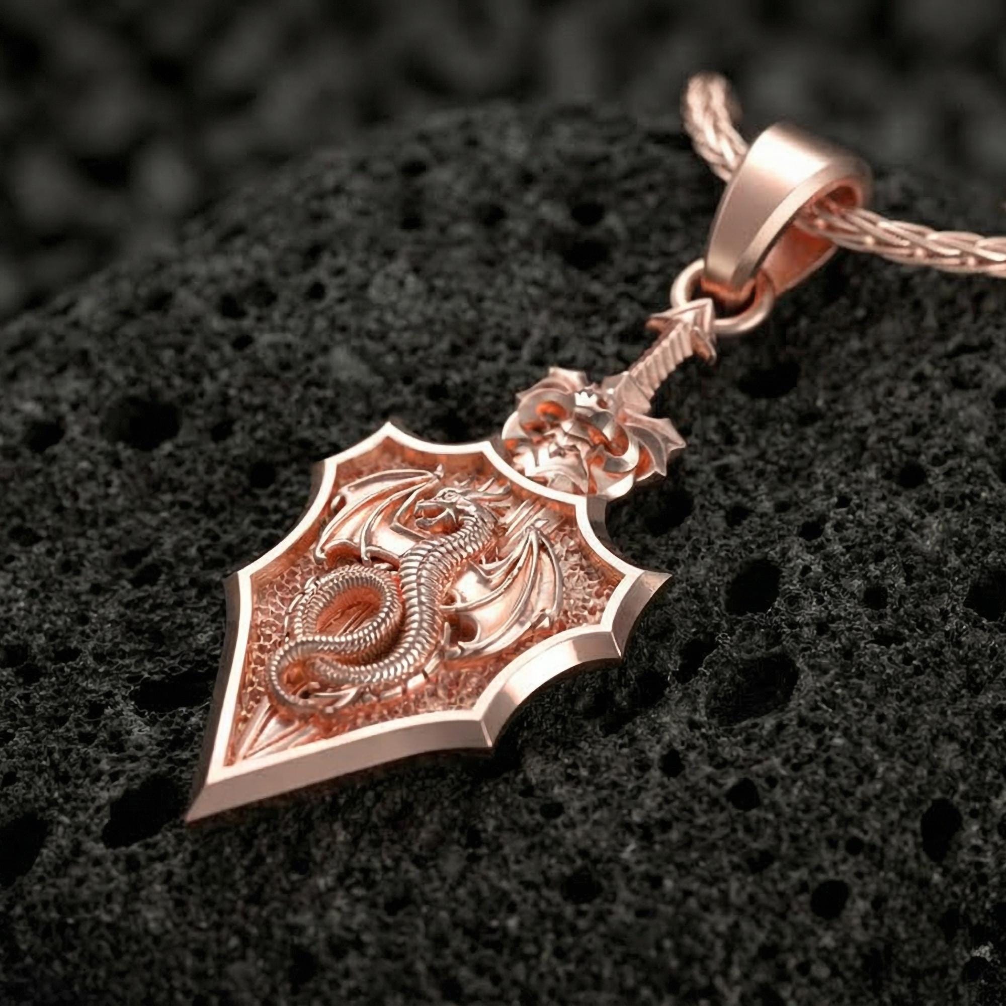 Rose gold plated dragon shield talisman necklace displayed on volcanic rock surface