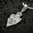 Load image into Gallery viewer, Polished silver dragon crest shield pendant photographed on volcanic stone background
