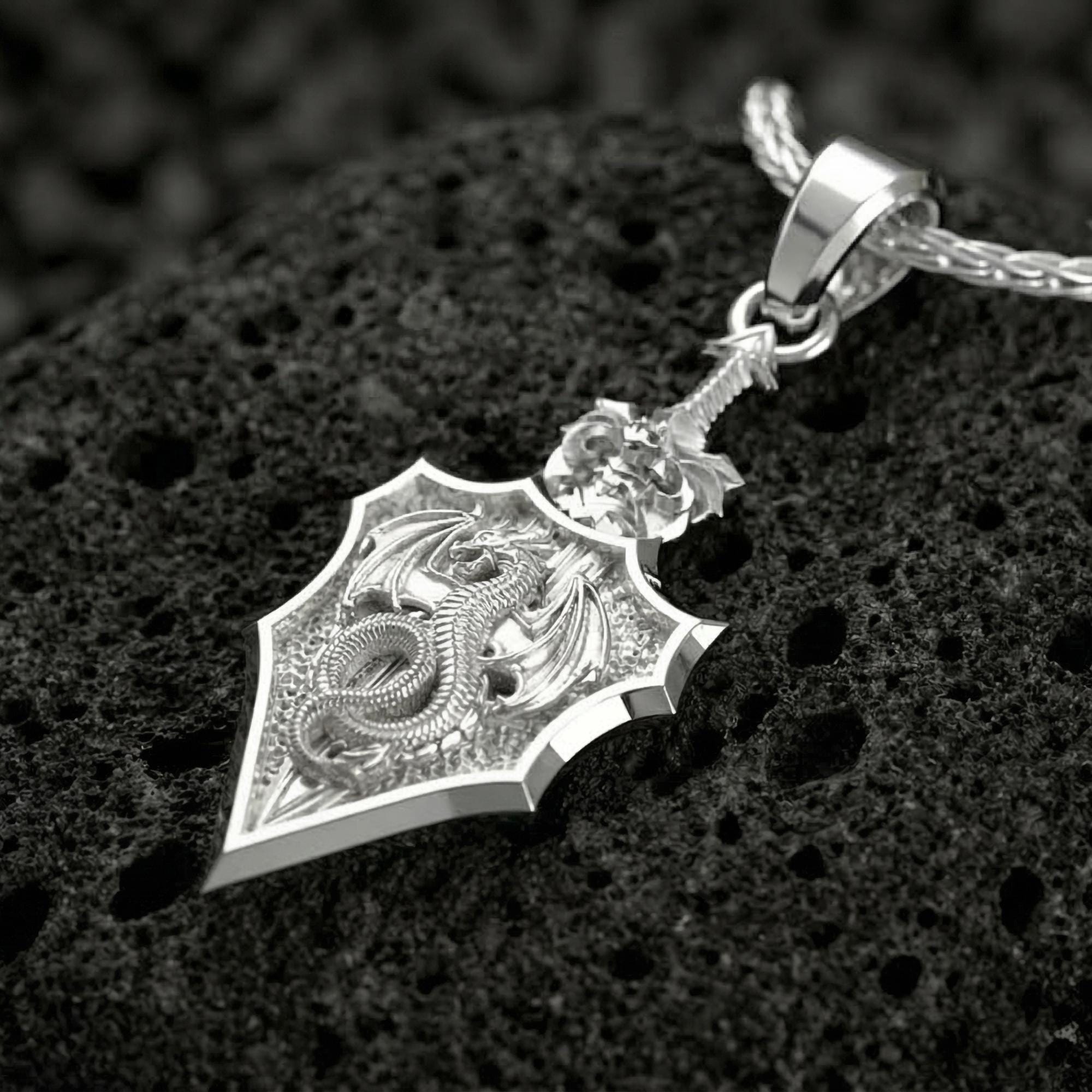 Polished silver dragon crest shield pendant photographed on volcanic stone background