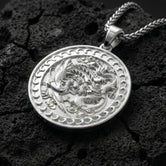 Polished silver dragon phoenix harmony pendant photographed on volcanic stone background