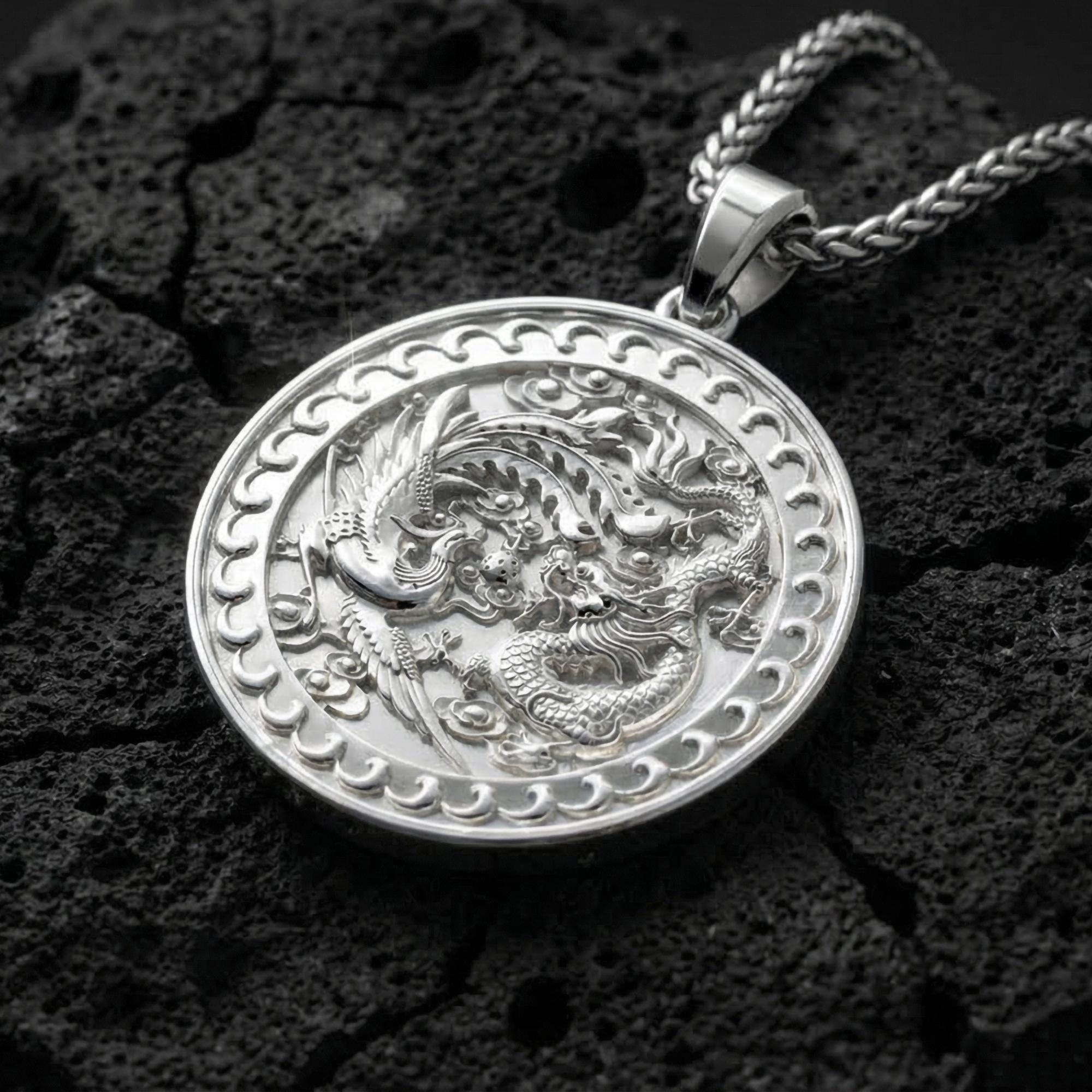 Polished silver dragon phoenix harmony pendant photographed on volcanic stone background