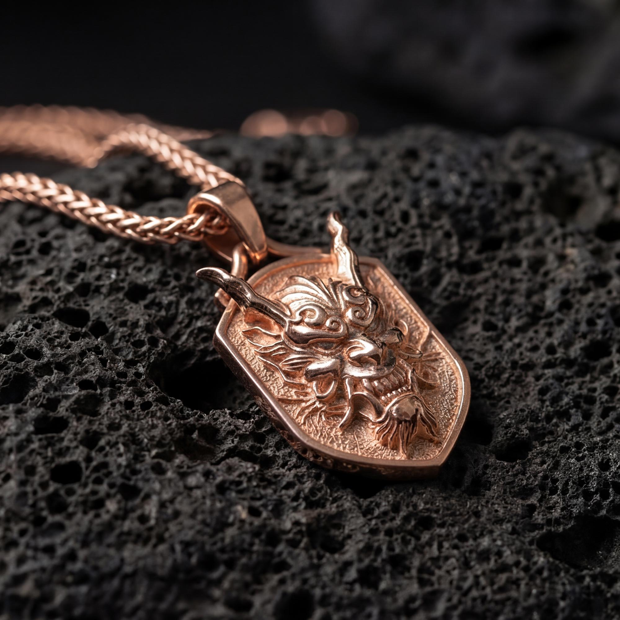 Rose gold plated oni mask dragon dog tag necklace presented on volcanic rock surface with dark mythic aesthetic