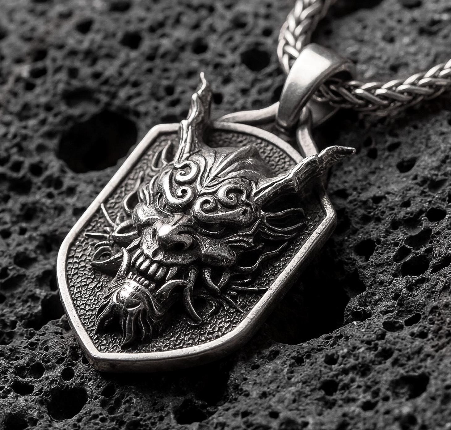 Oxidized oriental demon dragon dog tag pendant necklace photographed on volcanic rock with deep engraved oni mask detail
