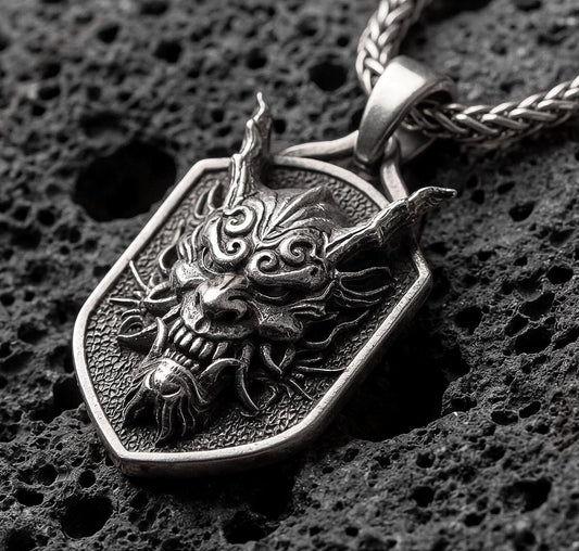 Oxidized oriental demon dragon dog tag pendant necklace photographed on volcanic rock with deep engraved oni mask detail