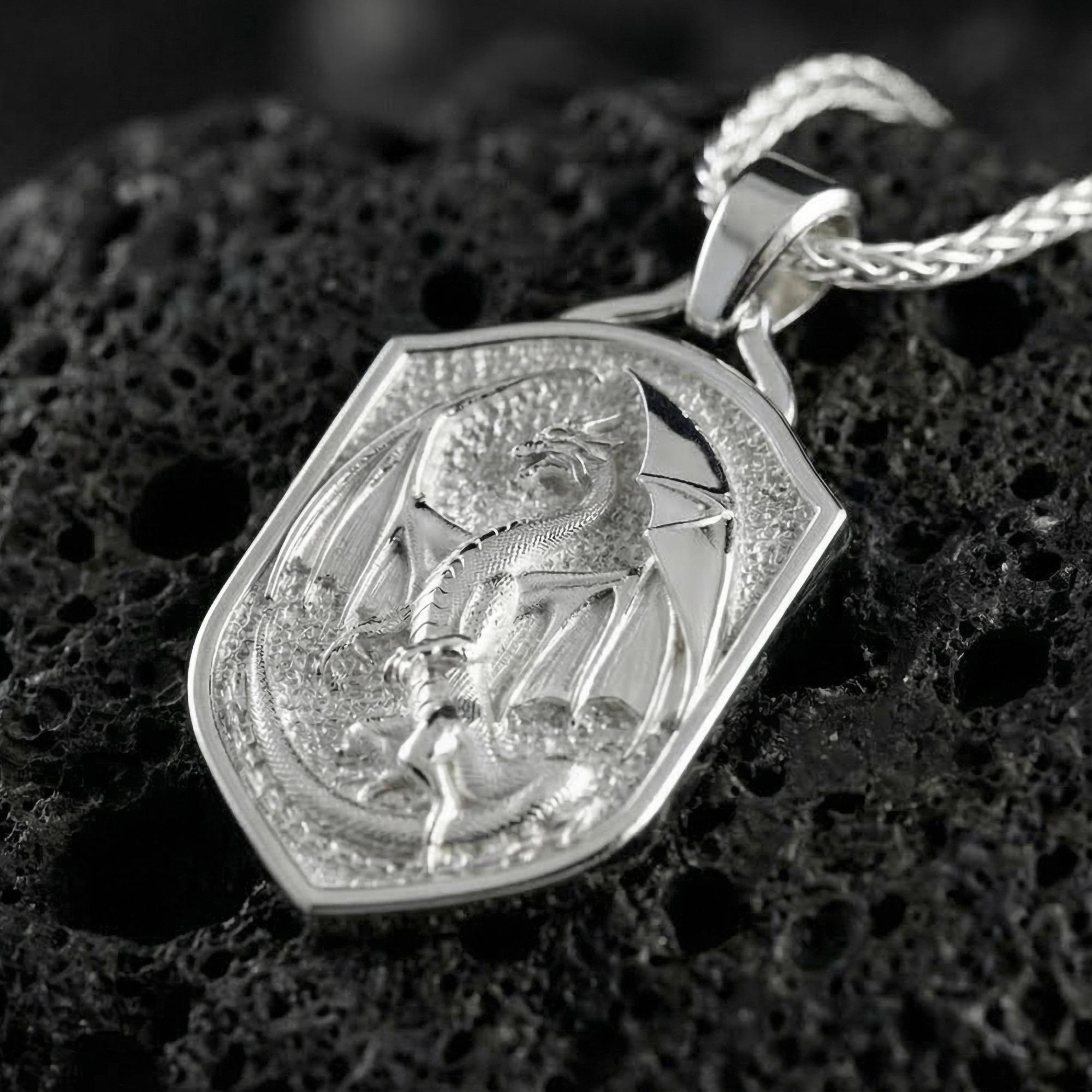 Polished silver gothic dragon shield pendant necklace displayed on volcanic stone background with sharp sculpted relief