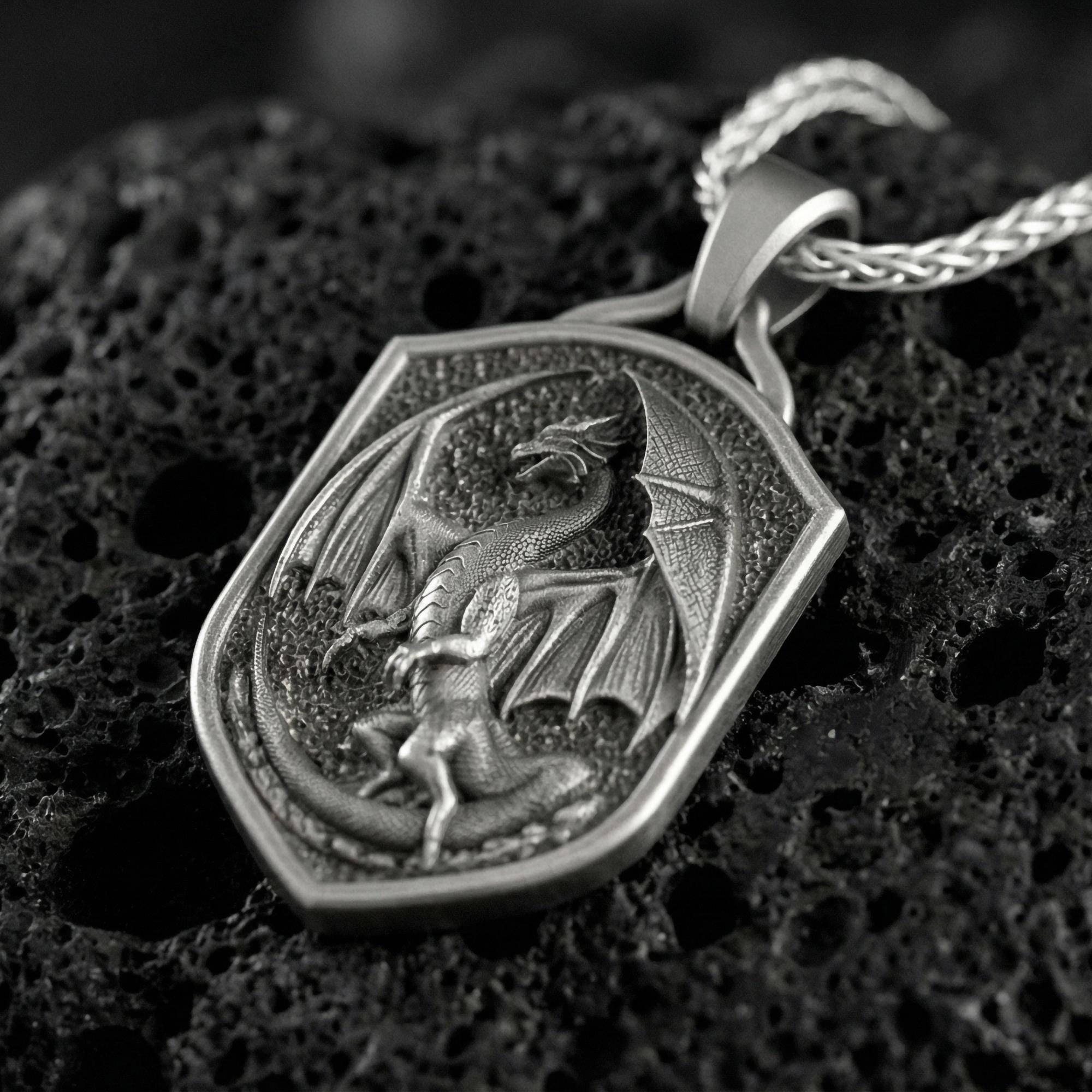 Oxidized fantasy shield dragon pendant necklace photographed on volcanic rock with deep engraved winged dragon detail