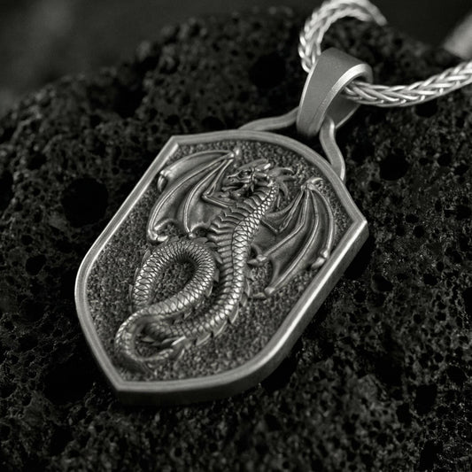 Oxidized coiled dragon shield pendant necklace photographed on volcanic rock with deeply engraved fantasy dragon detail