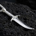 Load image into Gallery viewer, Polished silver fantasy dagger pendant necklace displayed on volcanic stone background with sharp gothic texture
