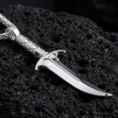 Polished silver fantasy dagger pendant necklace displayed on volcanic stone background with sharp gothic texture