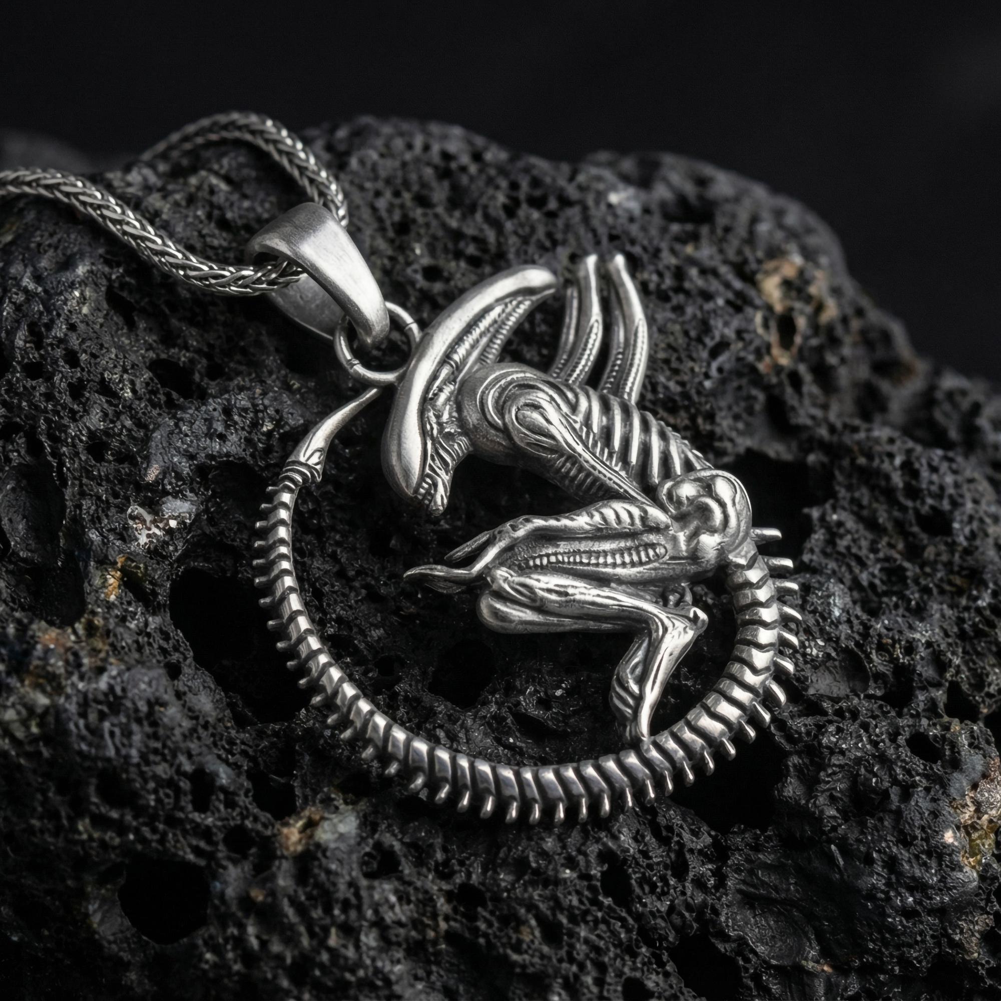 Oxidized alien xenomorph pendant necklace photographed on volcanic rock with biomechanical sci-fi horror detail