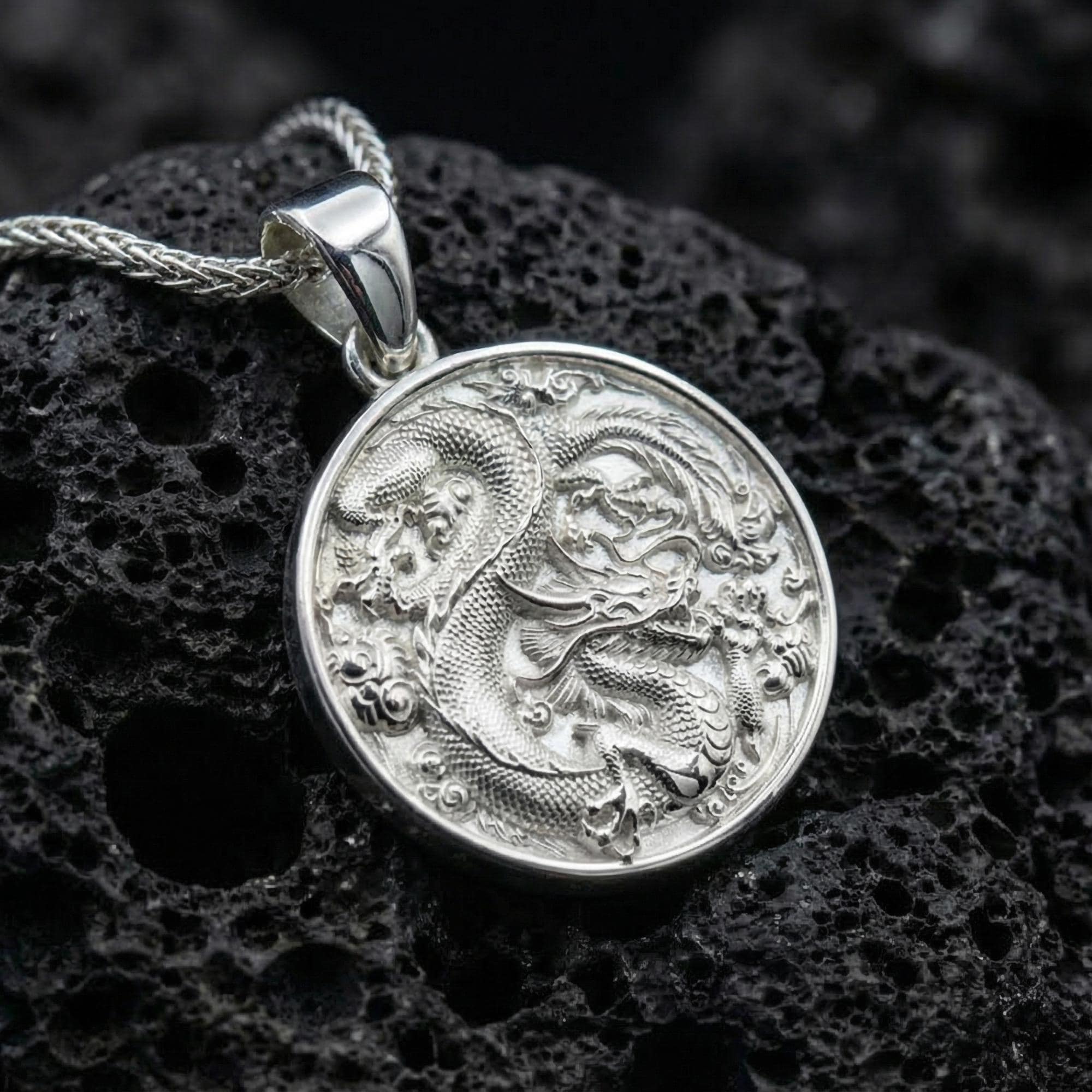 Polished silver dragon coin necklace featuring detailed mythical dragon relief on black volcanic stone