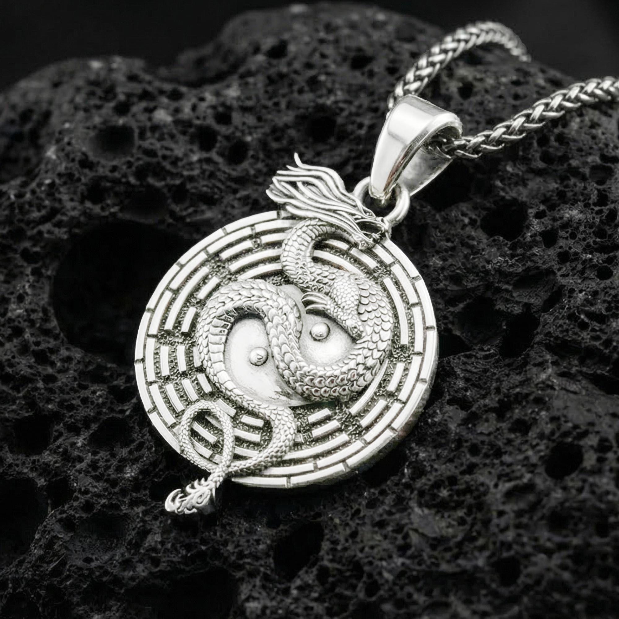 Polished silver yin yang dragon medallion necklace featuring taoist balance symbol on volcanic stone background