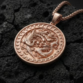 Rose gold plated yin yang dragon phoenix pendant displayed on volcanic rock surface