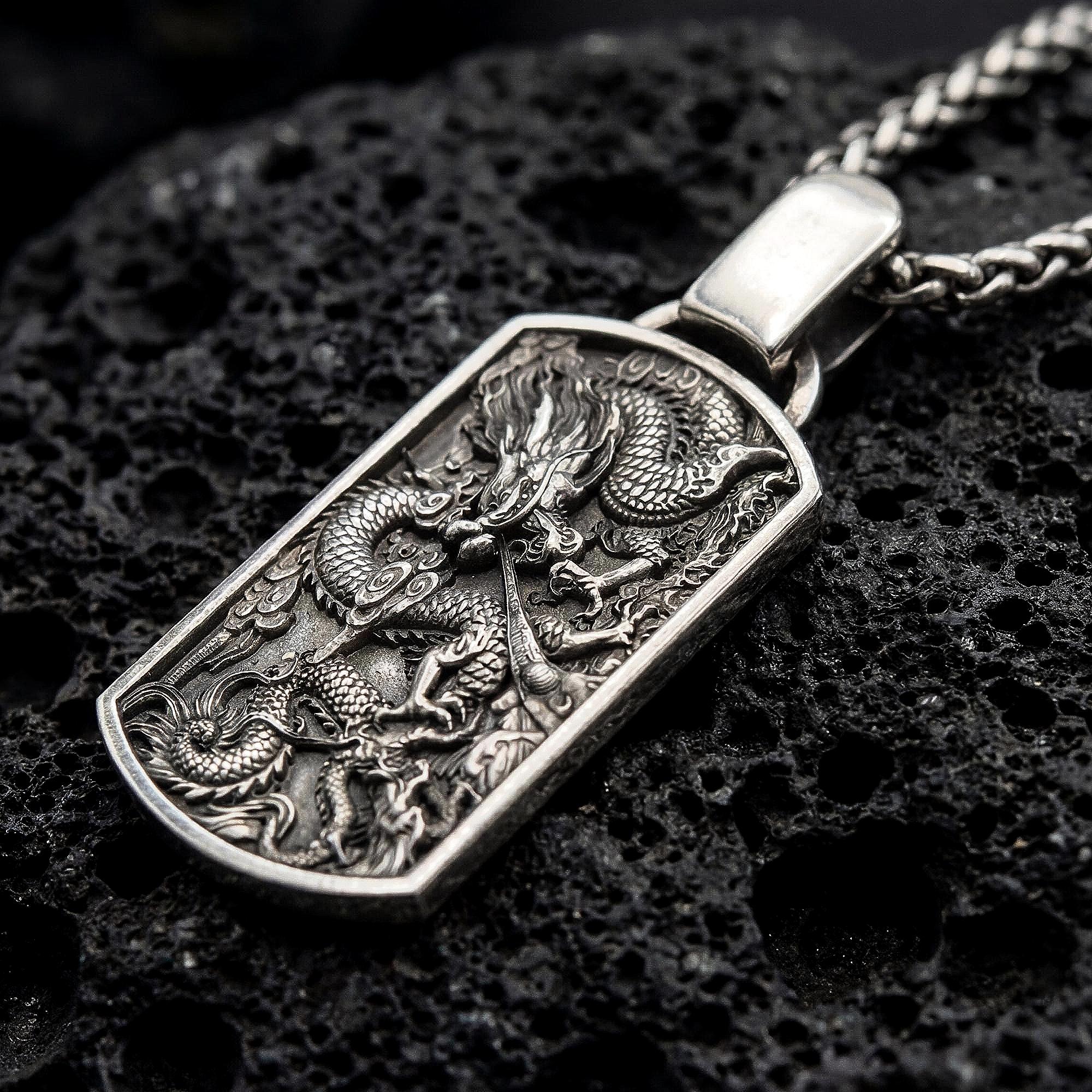 Oxidized chinese dragon dog tag pendant necklace photographed on volcanic rock with deep engraved detail