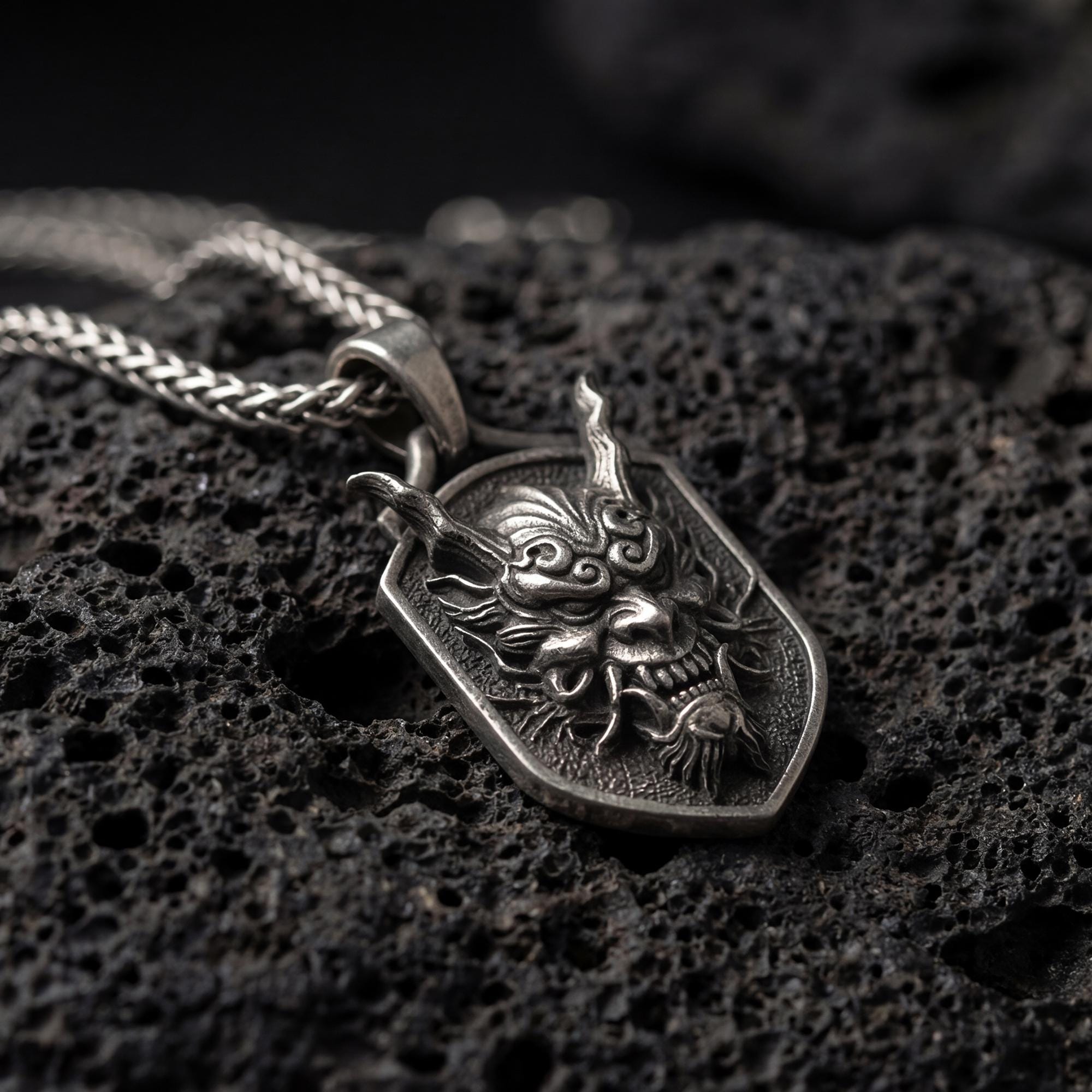 Oxidized oriental demon dragon dog tag pendant necklace photographed on volcanic rock with deep engraved oni mask detail