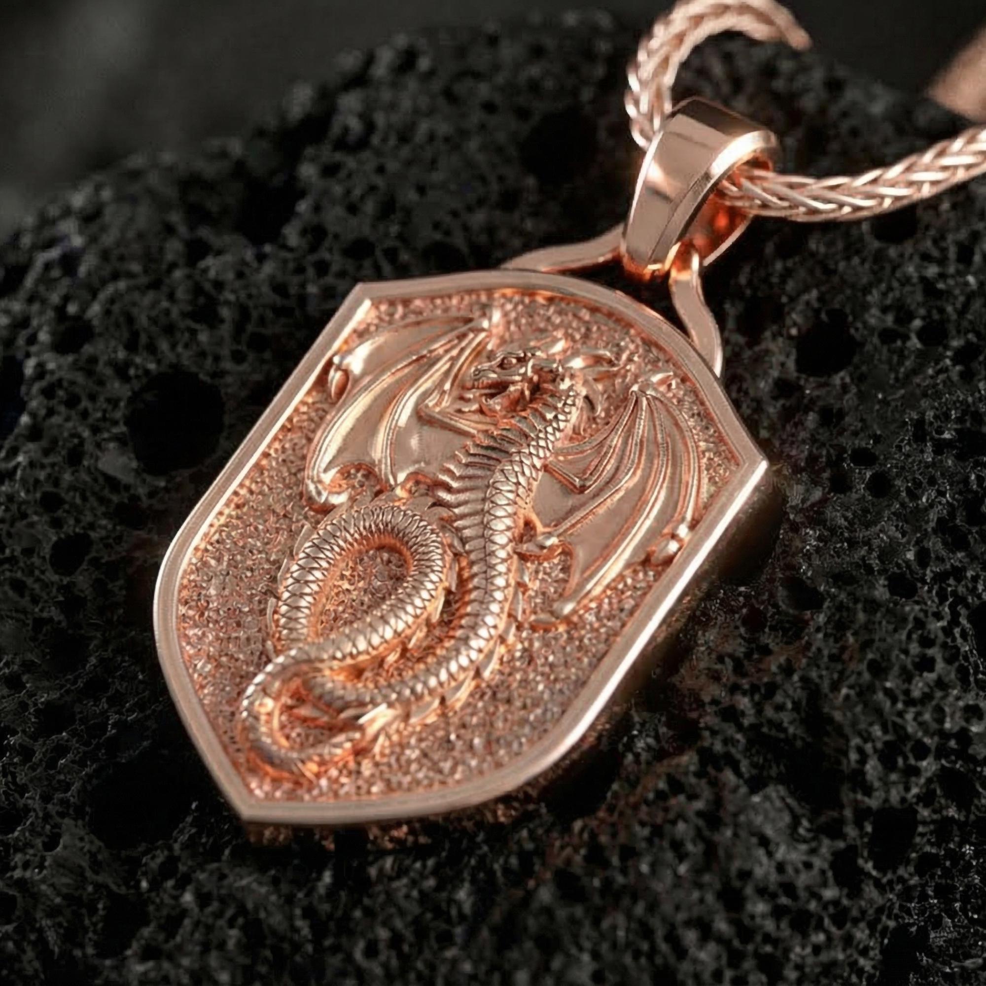 Rose gold plated coiled dragon shield necklace presented on volcanic rock surface with dark medieval aesthetic