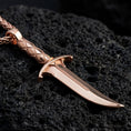 Load image into Gallery viewer, Rose gold plated gothic dagger pendant necklace presented on volcanic rock surface with cursed blade aesthetic
