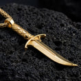 Load image into Gallery viewer, Gold plated Astarion inspired dagger pendant showcased on volcanic rock as dark fantasy vampire jewelry
