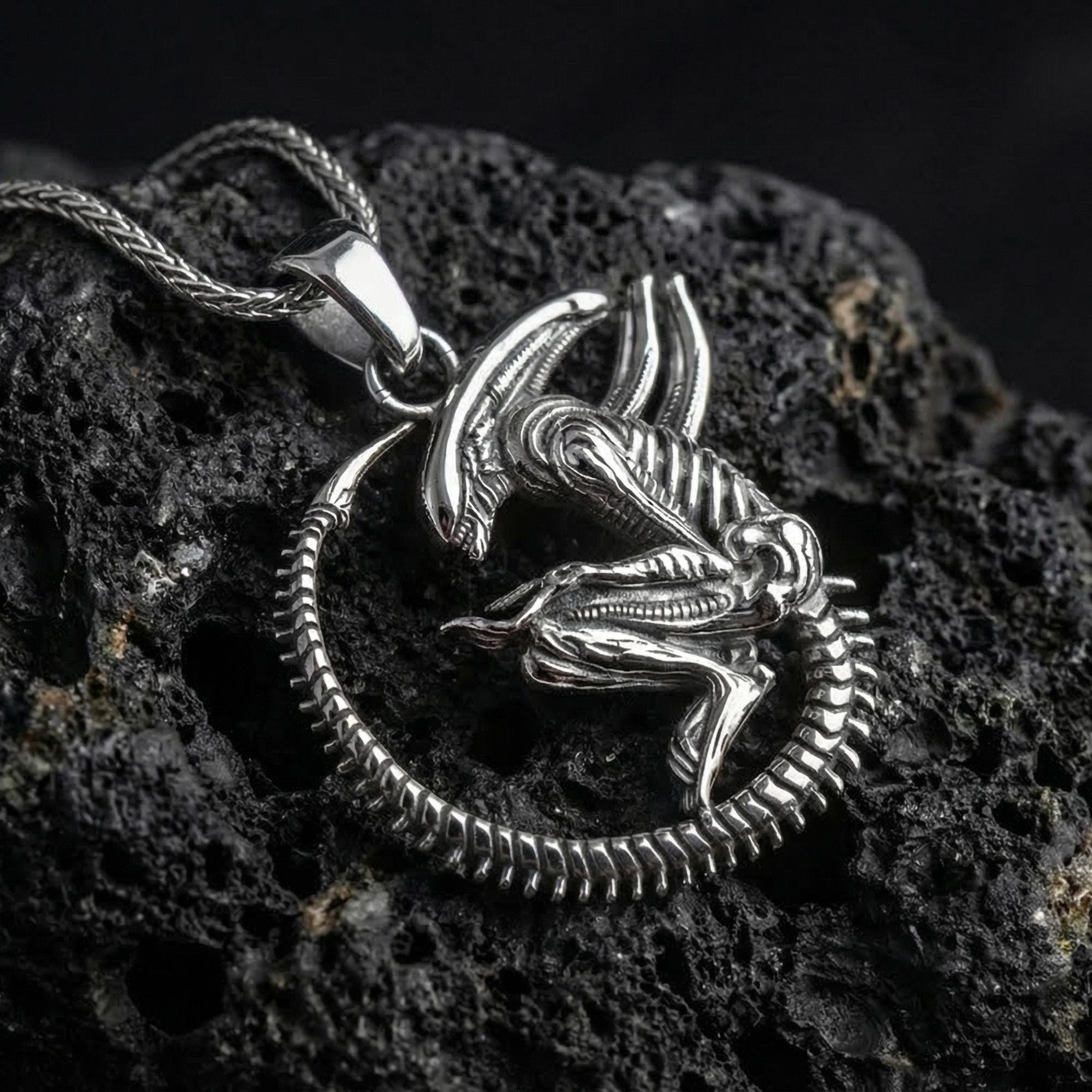 Polished silver xenomorph alien pendant necklace displayed on volcanic stone background with sharp sculpted relief