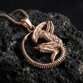 Load image into Gallery viewer, Rose gold plated xenomorph creature pendant necklace presented on volcanic rock surface with futuristic horror aesthetic
