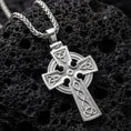 Load image into Gallery viewer, Polished silver celtic trinity knot cross necklace displayed on volcanic stone background
