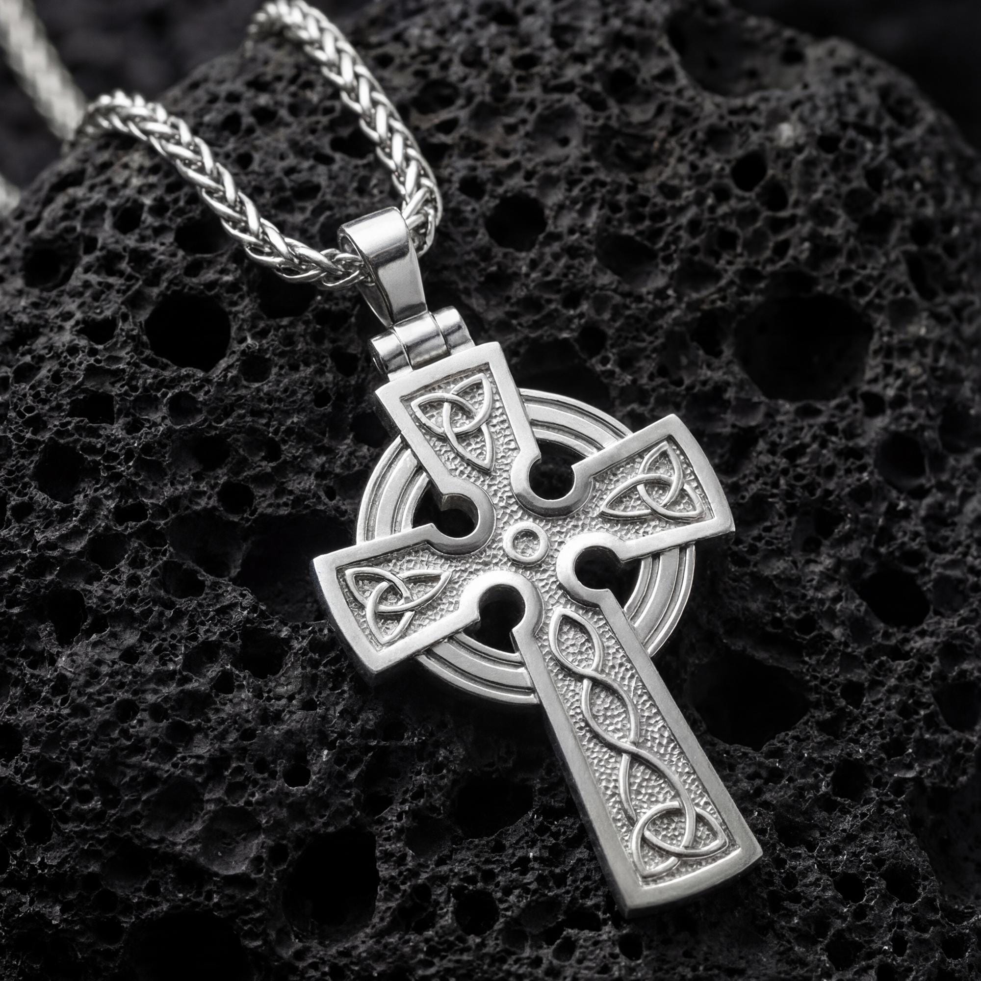 Polished silver celtic trinity knot cross necklace displayed on volcanic stone background