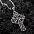 Load image into Gallery viewer, Oxidized celtic cross pendant necklace photographed on volcanic rock with trinity knot engravings
