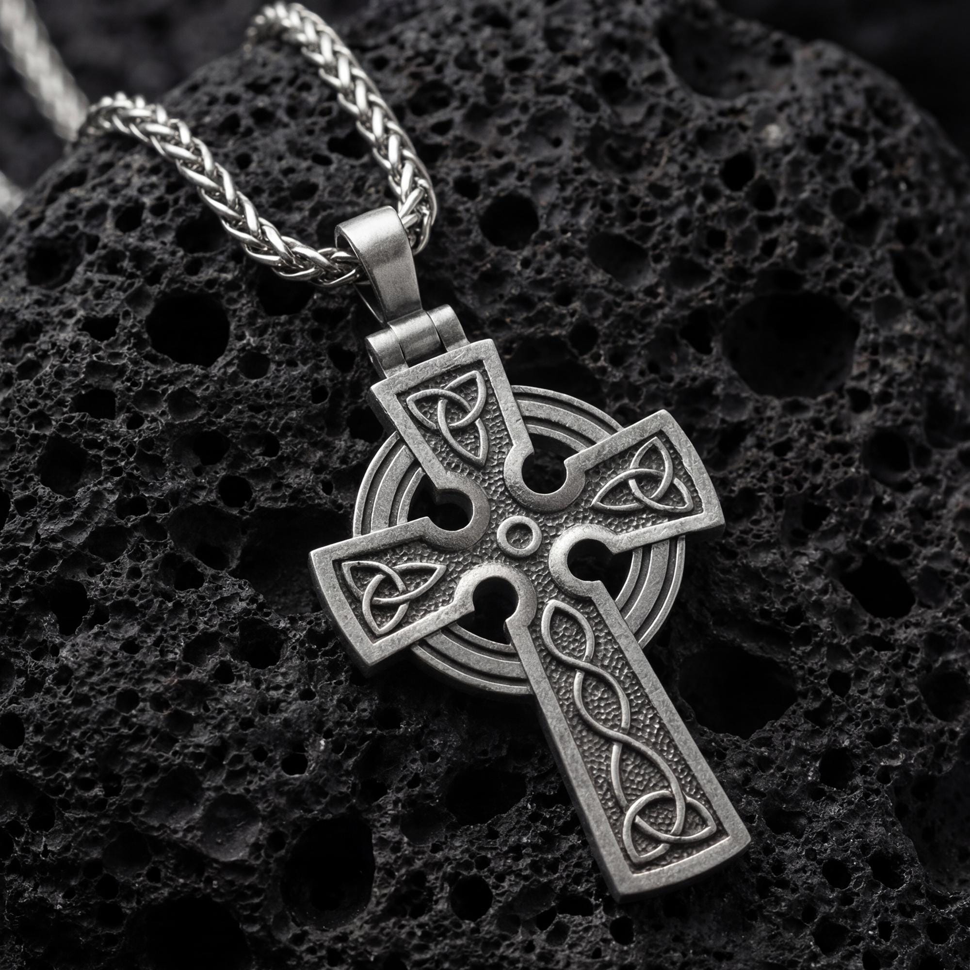 Oxidized celtic cross pendant necklace photographed on volcanic rock with trinity knot engravings