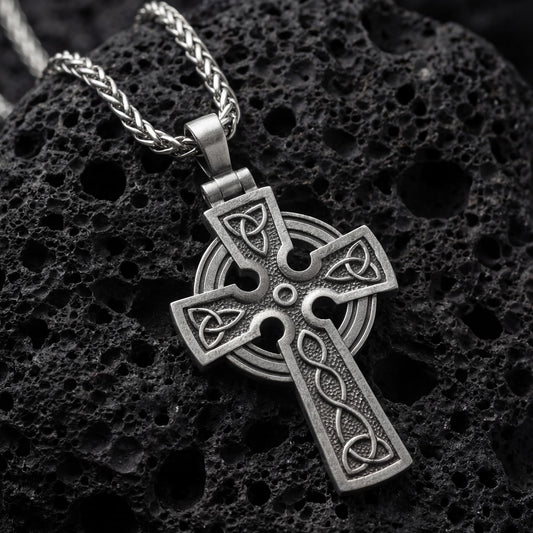 Oxidized celtic cross pendant necklace photographed on volcanic rock with trinity knot engravings