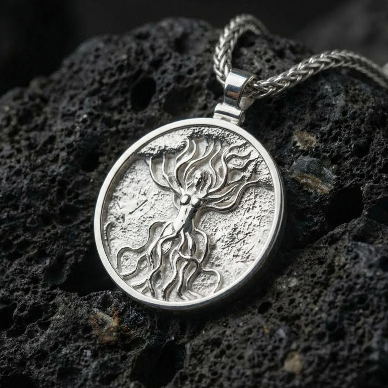 Polished silver sacred tree goddess pendant necklace displayed on volcanic stone background with flowing organic detail